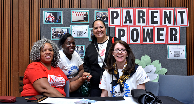 Four people smiling in front of a display board with 'Parent Power' and photos. 
