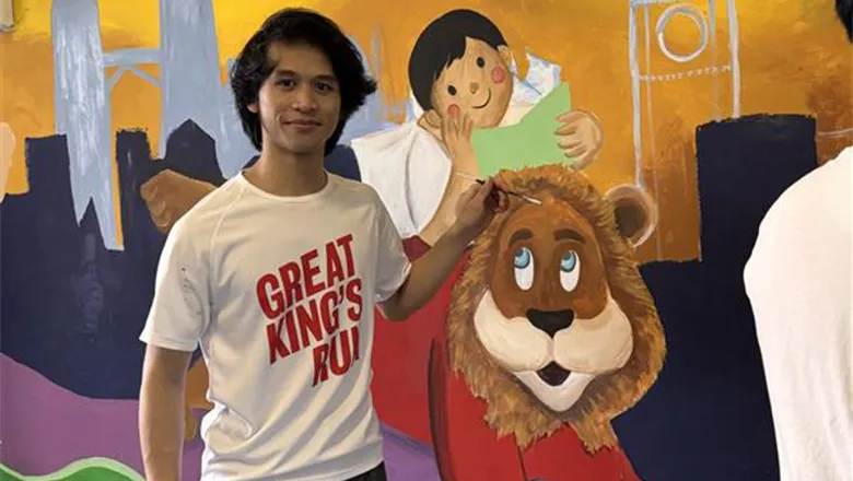 A young man with dark hair puts the finishing touches to a mural that features a playful version of the King’s mascot, Reggie the Lion