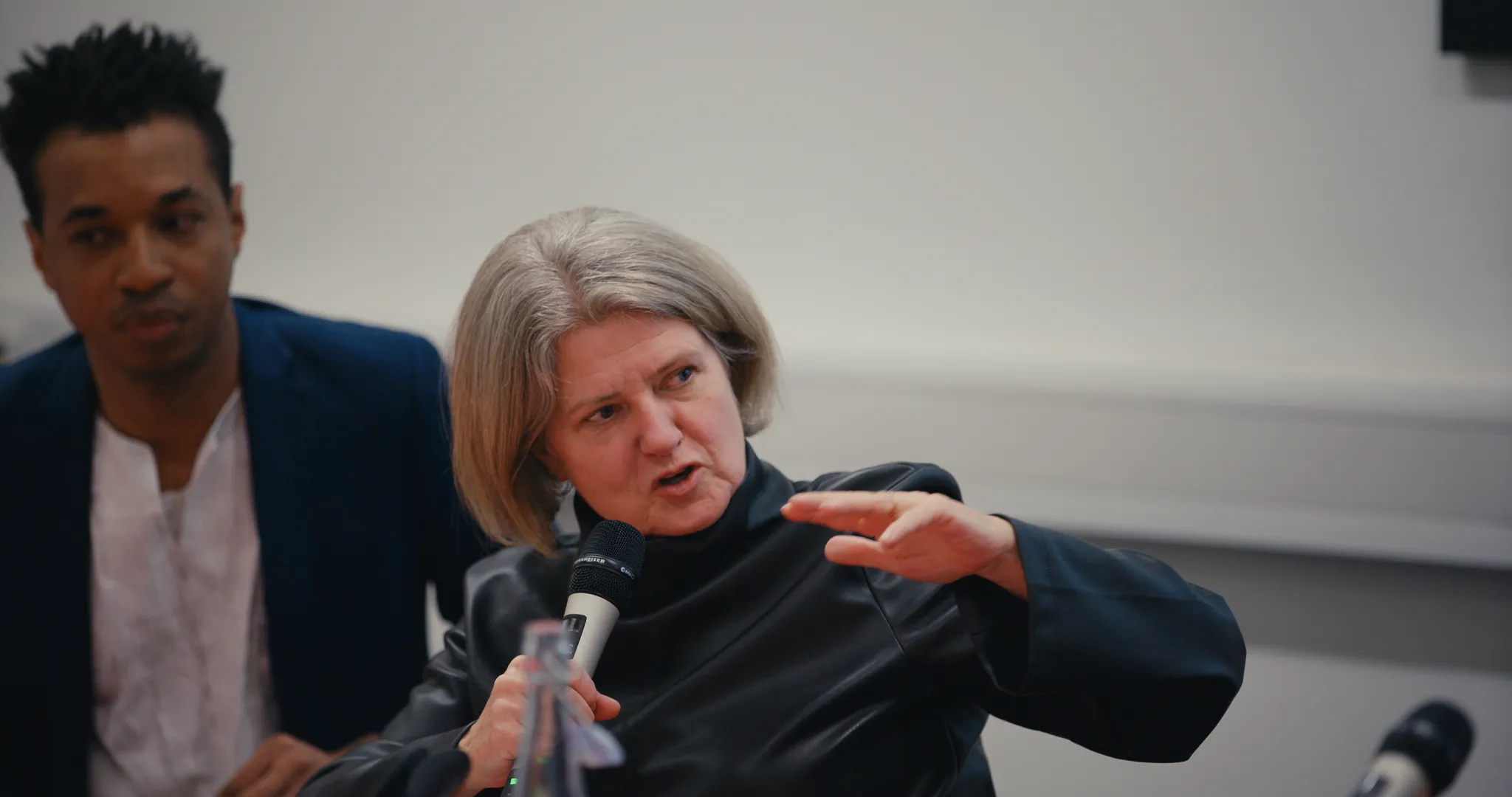 Professor Sally Marlow speaking into microphone, seated to the right of Dr Ricardo Twumasi