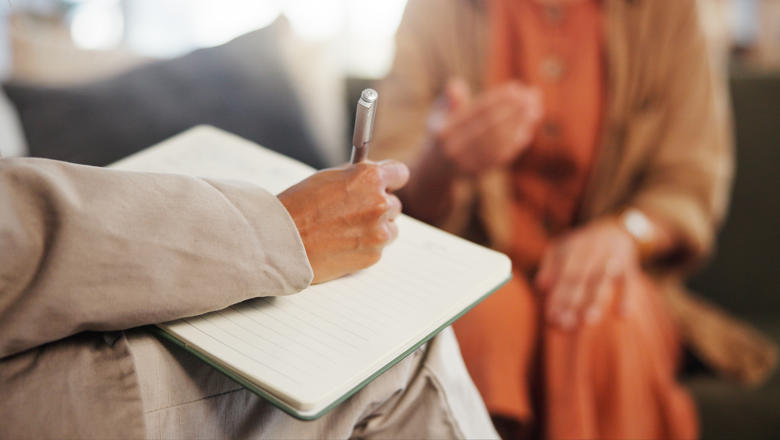 A person writing on a note pad as another person speaks in the background