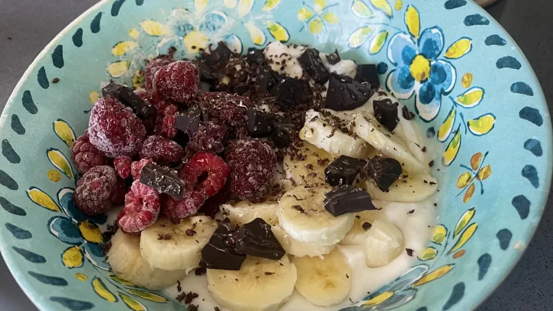 A bowl with yogurt, banana pieces, and cheeries.